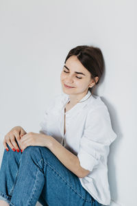 Smiling young woman sitting against white background