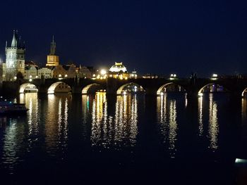 Illuminated bridge over river by buildings against sky at night