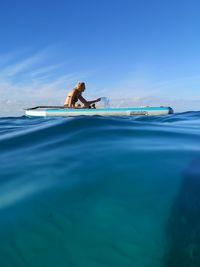 Side view of man floating on sea against blue sky