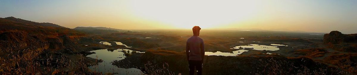 Rear view of woman standing on landscape against sunset sky
