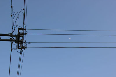 Low angle view of electricity pylon against clear blue sky