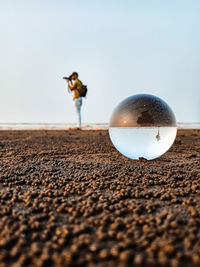 Close-up of crystal ball on sand against clear sky