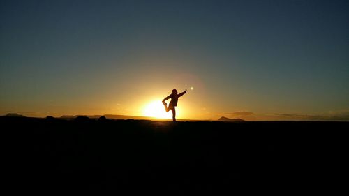 Silhouette man with hand raised standing on field against sky during sunset