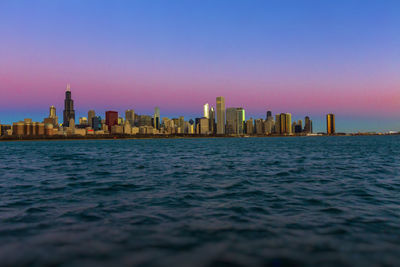 Sea by modern buildings in city against sky