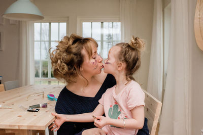 Mother kissing daughter whilst they play with make up at home