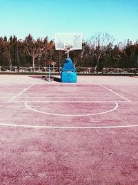 Boy playing basketball court against blue sky