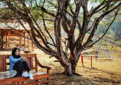 Smiling woman sitting on bench by tree on field