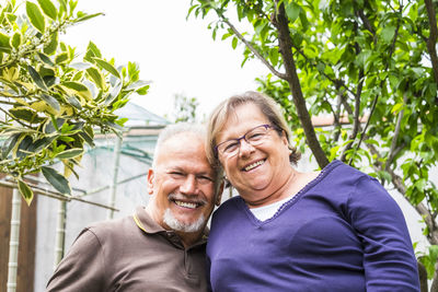 Portrait of smiling man and woman standing by trees in yard 