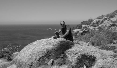 Man on rock by sea against clear sky