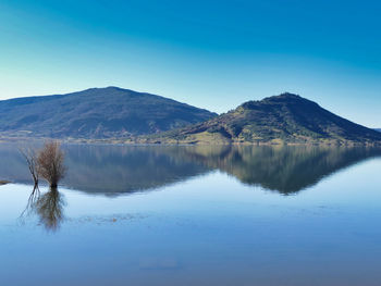 Scenic view of lake and mountains against clear blue sky