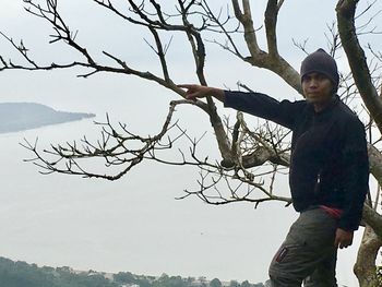 Portrait of man standing on bare tree against sky