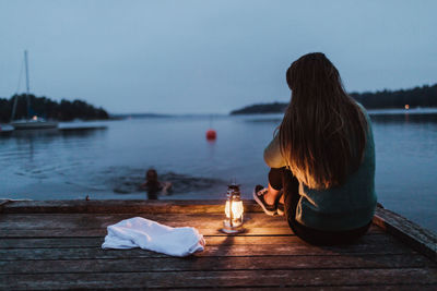 Rear view of woman sitting by lake against sky