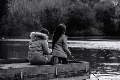 Rear view of couple sitting on pier over lake