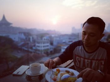 Man having food and drink at outdoor restaurant against cityscape