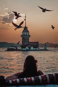 Rear view of woman sitting on boat on sea against sky during sunset