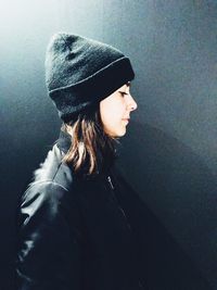 Side view of young woman wearing hat standing against wall