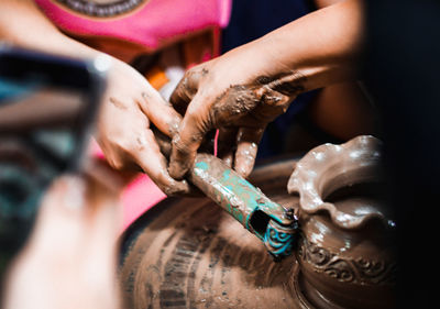 Cropped hand of man assisting female friend making pot in workshop