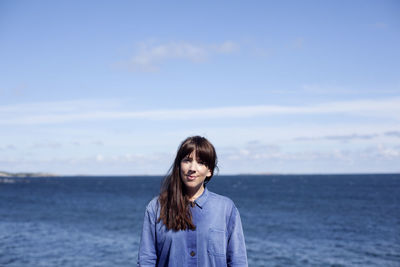 Portrait of smiling young woman standing in sea against sky