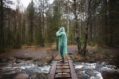 Man wearing raincoat while standing on footbridge in forest