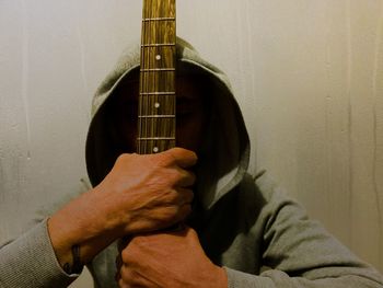 Midsection of man holding guitar against wall