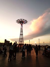 Silhouette people at amusement park against sky during sunset