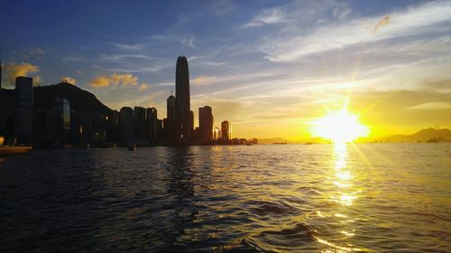 Silhouette two international finance center by victoria harbour against bright sky during sunset