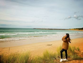 Rear view of man standing on beach against sky