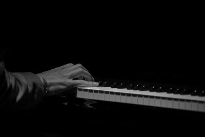 Midsection of person playing piano against black background