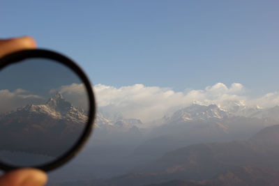 Cropped image of hand holding lens against snowcapped mountain