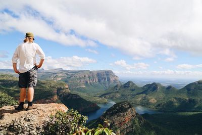 Rear view of man standing on rock while looking at valley against sky