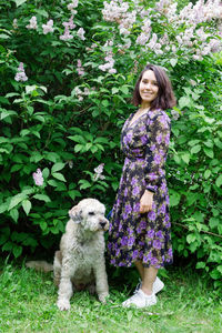 Portrait of woman with dog on grass against plants