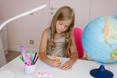 Girl sits at home at a table and write in a notebook, completing a learning task or repeating