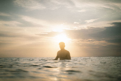 Man in swimming pool against sea during sunset