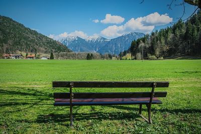 Empty bench on field by mountains against sky