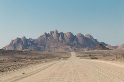 Dirt road in desert against clear sky