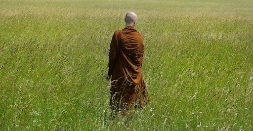 Rear view of monk standing on grassy field