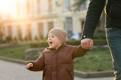 A happy three year old son walks hand in hand with his dad in the city on a sunny spring day. 