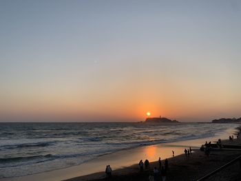 People on beach against sky during sunset