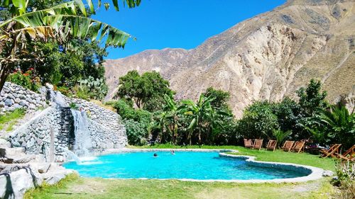 Swimming pool by trees against blue sky