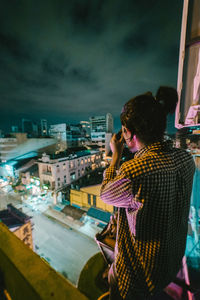 Rear view of man standing on illuminated city against sky at night