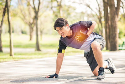 Full length of young man suffering from chest pain on road at park