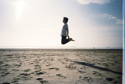 Man jumping on beach against sky