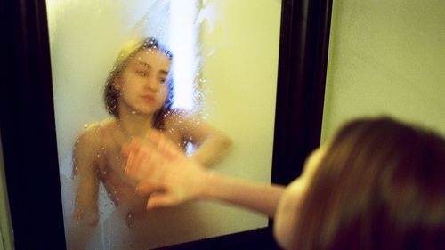 The beautiful woman with wet hair looks in a mirror in a bathroom