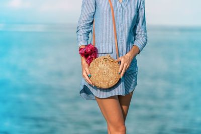 Midsection of woman with bag standing against sea