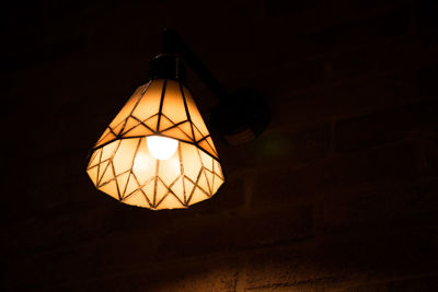 Low angle view of illuminated lamp against wall in room
