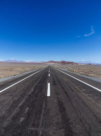 Road passing through desert against blue sky