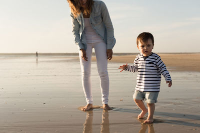 Low section of mother with son walking at beach