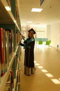 Full length of woman standing by bookshelf in library