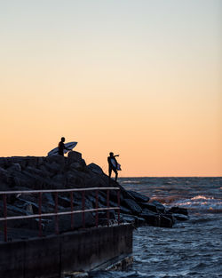 People on sea against clear sky during sunset