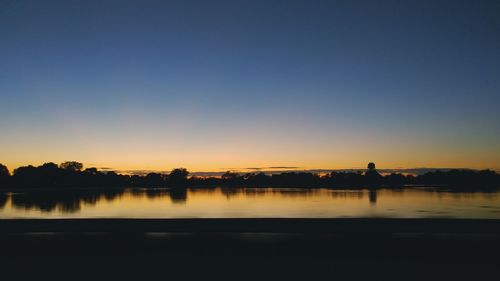 Silhouette calm lake against clear sky during sunset